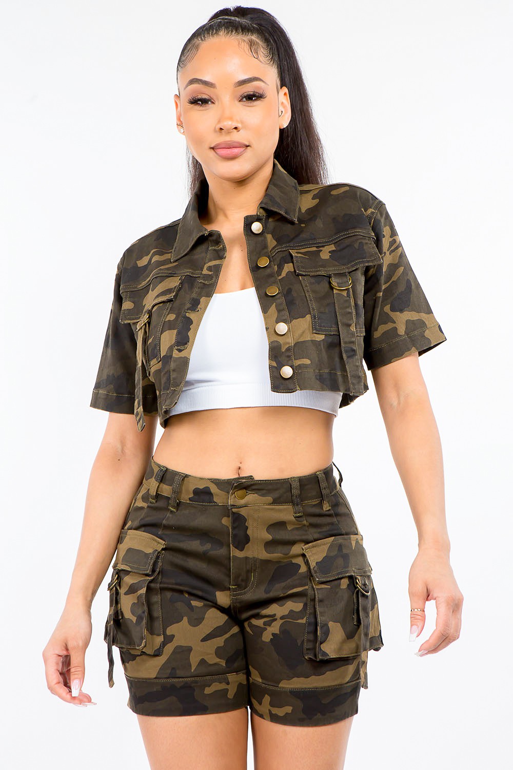 Person wearing a trendy outfit featuring the American Bazi Full Size Camouflage Short Sleeve Cropped Jacket and matching shorts, with a white crop top underneath, standing against a plain white background.