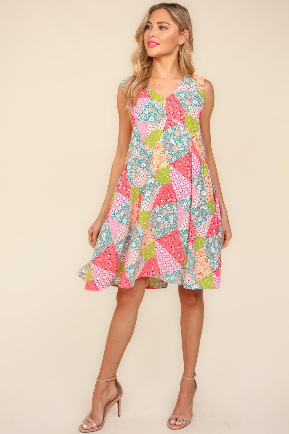 A woman in a Haptics Full Size Babydoll Floral Patchwork Dress with side pockets and nude heels stands against a plain background.