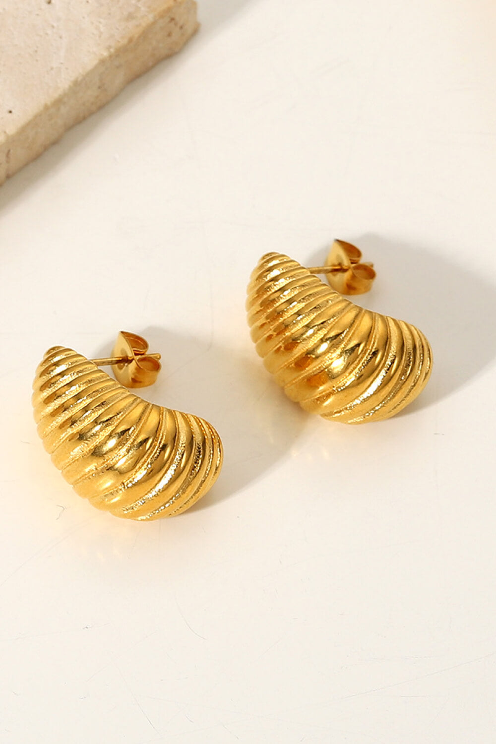 A pair of Shell Shore Spiral Stud Earrings, gold-plated with a ribbed, crescent shape and post-butterfly clasps on a white background.