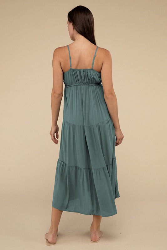 A woman wearing a teal woven sweetheart neckline tiered cami midi dress and sandals, standing against a neutral background.
