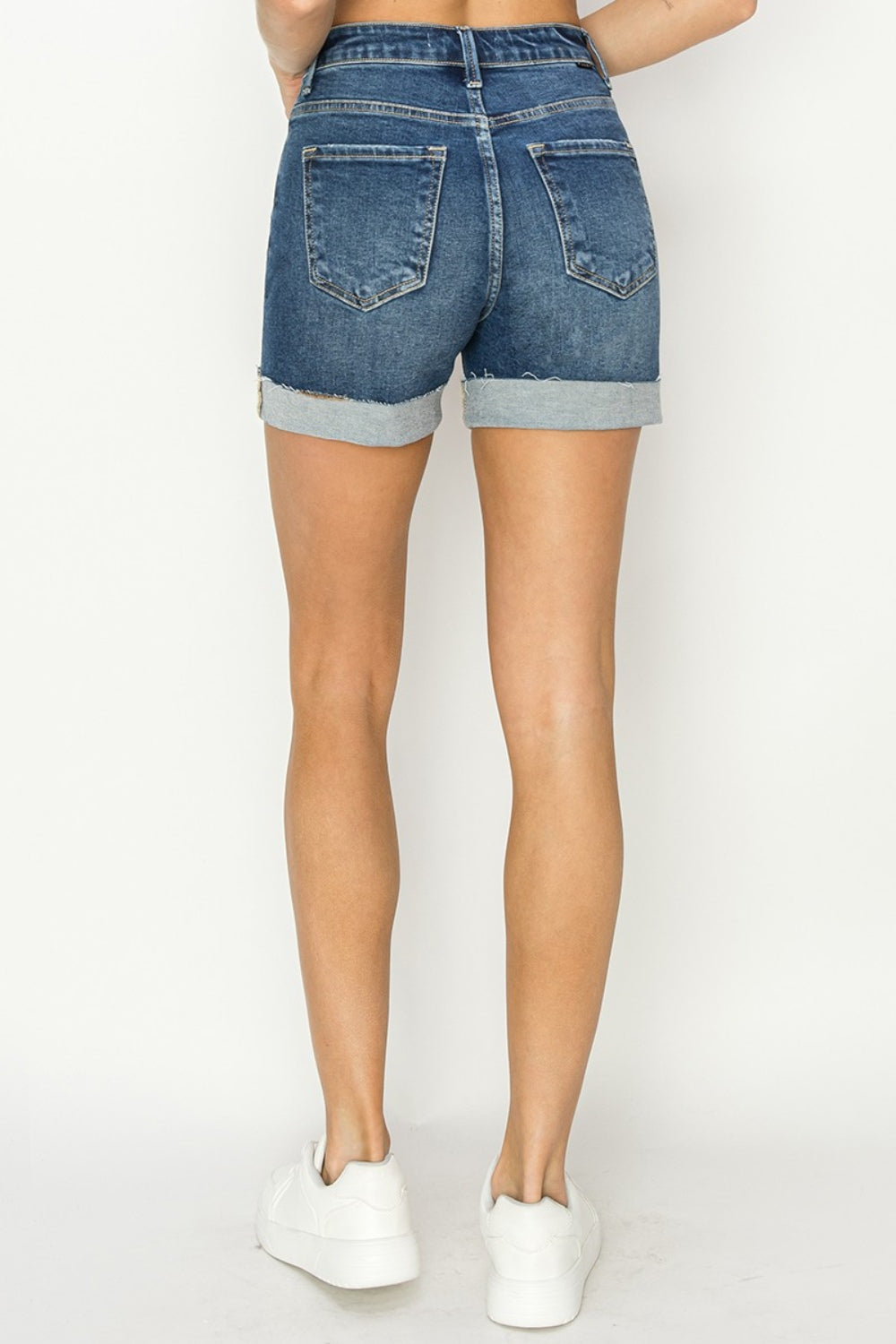 Person wearing RISEN High Rise Cuffed Denim Shorts with frayed hems, standing against a plain background. This chic and classic look is perfect for your summer wardrobe.