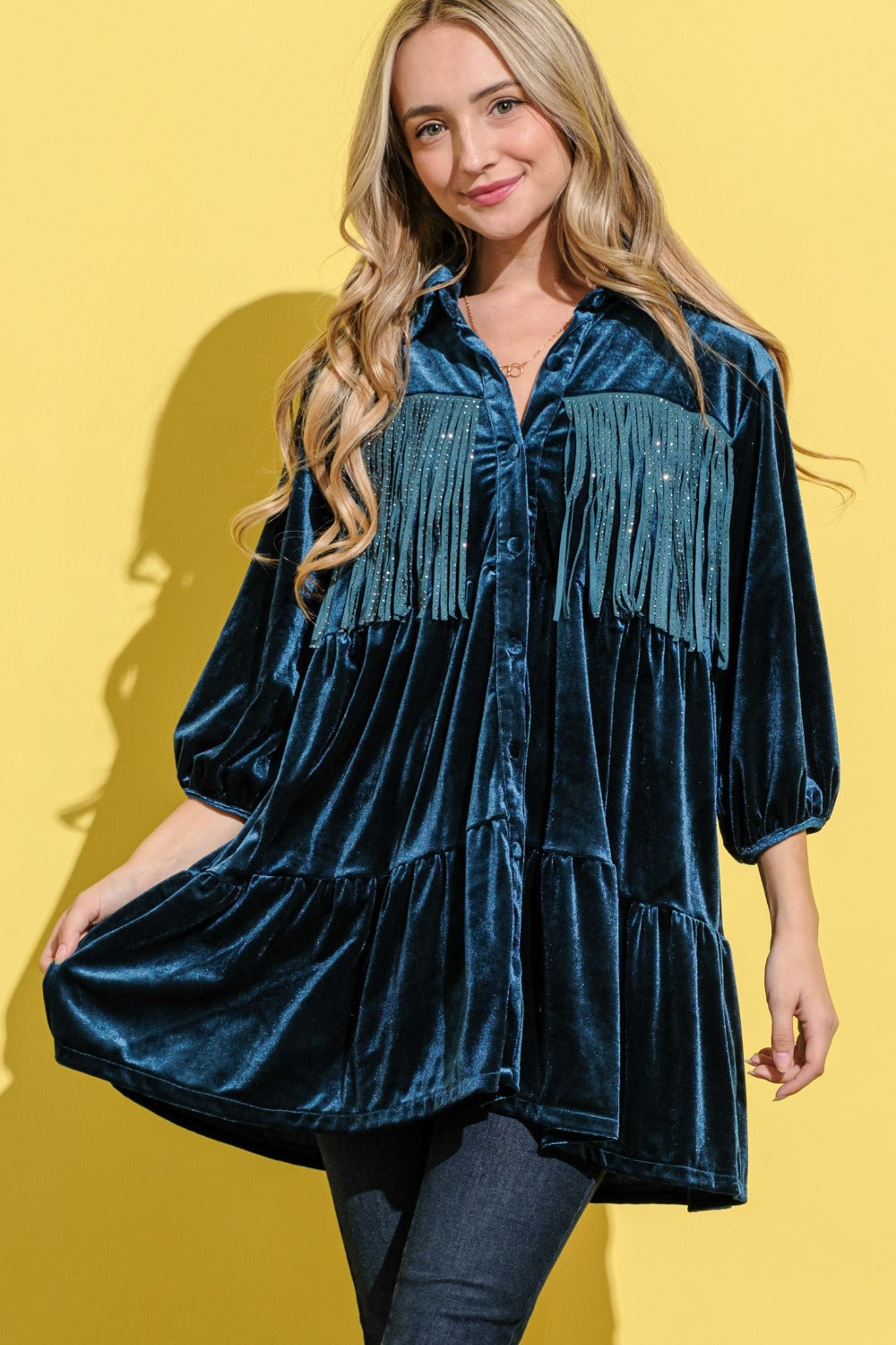 A woman in the And The Why Fringe Detailed Velvet Shirt Dress with a tailored fit and button-up front, wearing jeans, stands against a yellow background.