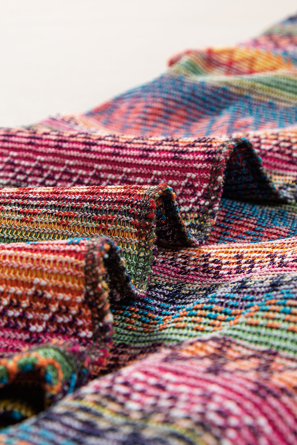 A person stands with hands in the pockets of their denim shorts, wearing a colorful Rose Red Ethnic Wavy Pattern Drop Shoulder Knit Top and a white shoulder bag.