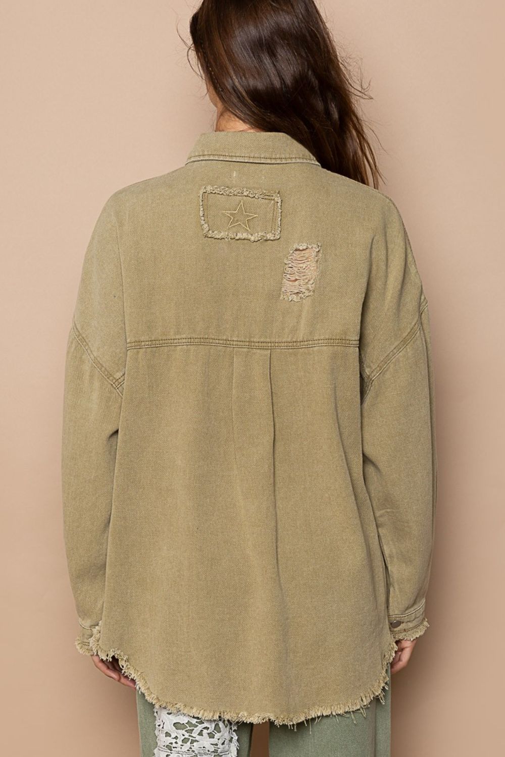 A woman with long hair wears a POL Button Down Raw Hem Distressed Shacket in khaki and matching pants, posing confidently against a beige background.