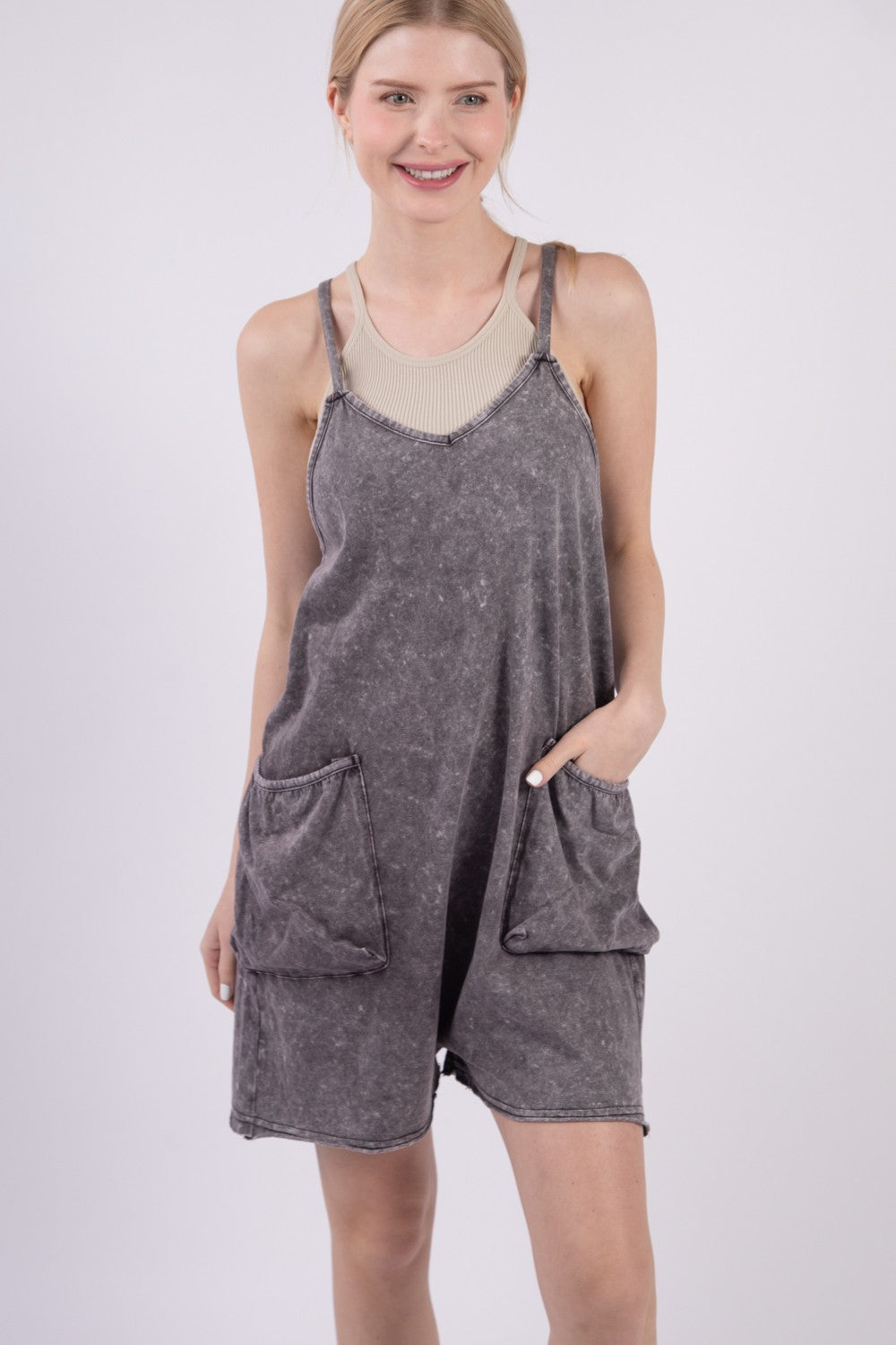 A person smiling against a plain background is wearing the VERY J V-Neck Sleeveless Washed Romper in gray, featuring two front pockets.