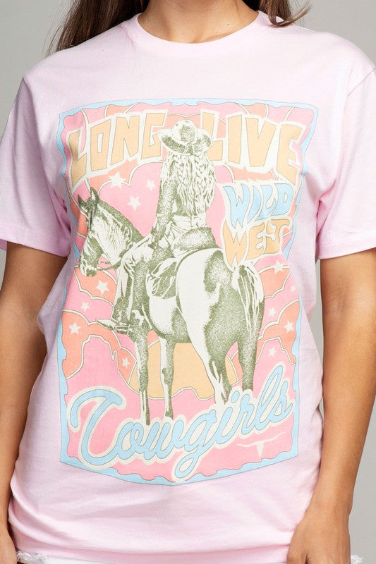 A woman wearing the Long Live Cowgirls Graphic Top with a Western print and white denim shorts poses with one hand on her hip.