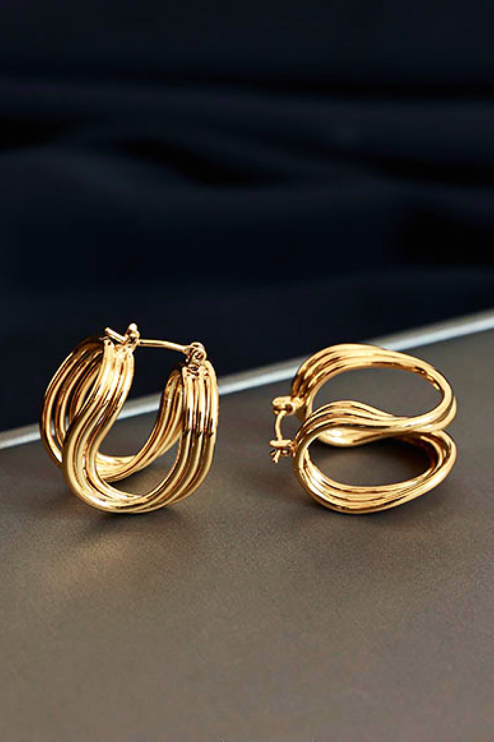 The U-Shaped Hoop Earrings feature a layered, wavy design on a light background, making them a stunning addition to any jewelry collection. These exquisite brass earrings showcase elegant craftsmanship, perfect for both casual and formal occasions.