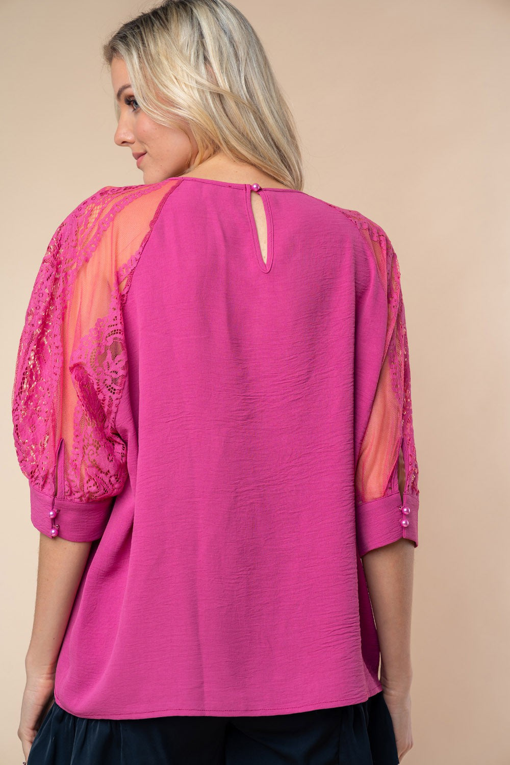 A person stands against a neutral background, wearing the White Birch round neck blouse with vibrant pink lace half sleeves.