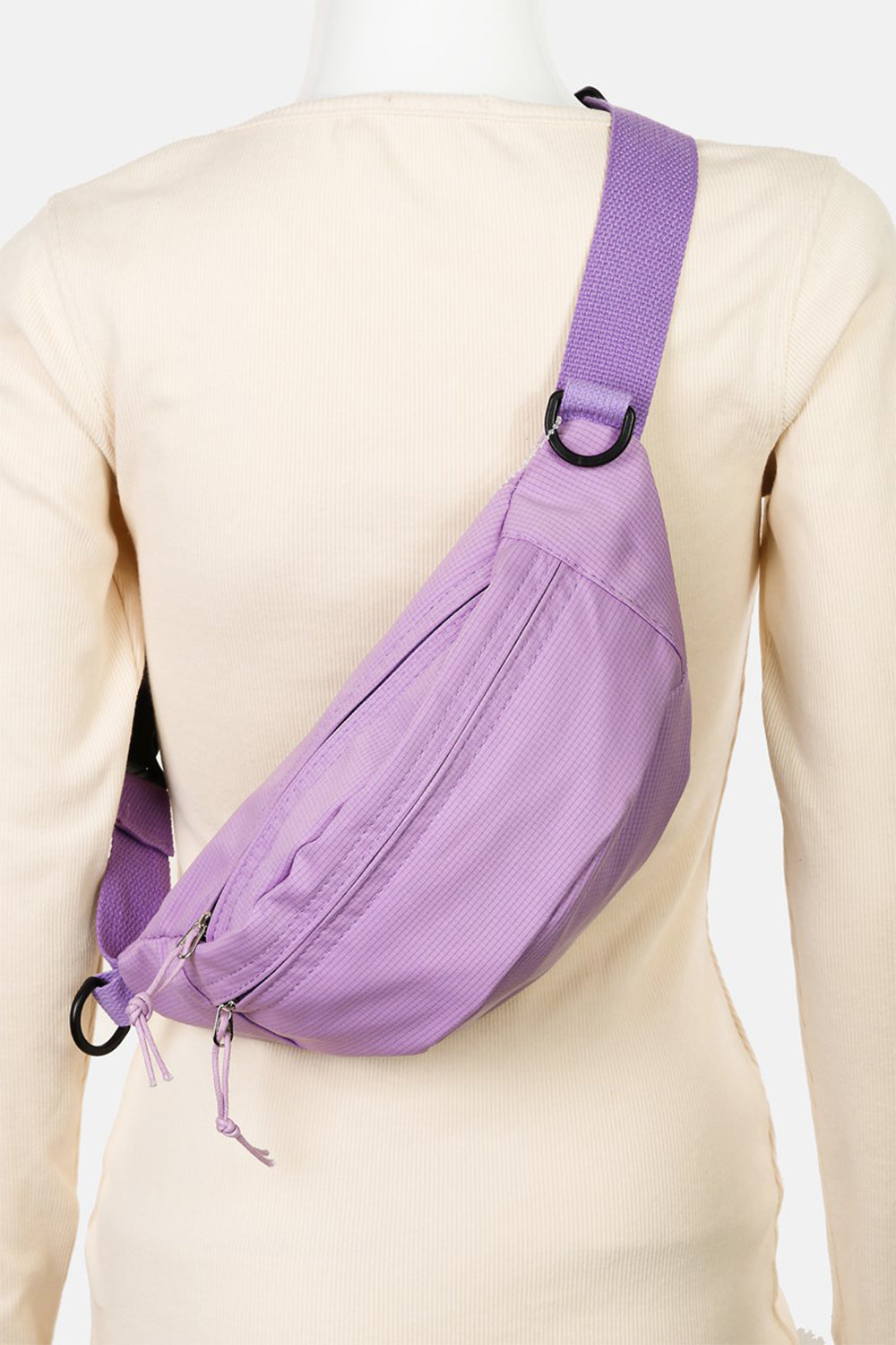 A woman in a black sleeveless top and beige pants stands against a light background, showcasing her versatile accessory—the Fame Adjustable Strap Sling Bag, crafted from durable materials.