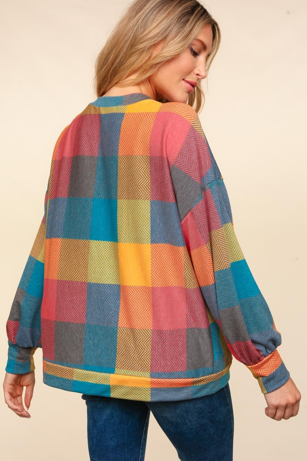 A woman wearing a stylish Haptics Round Neck Color Block Plaid Top and blue jeans poses against a beige background.