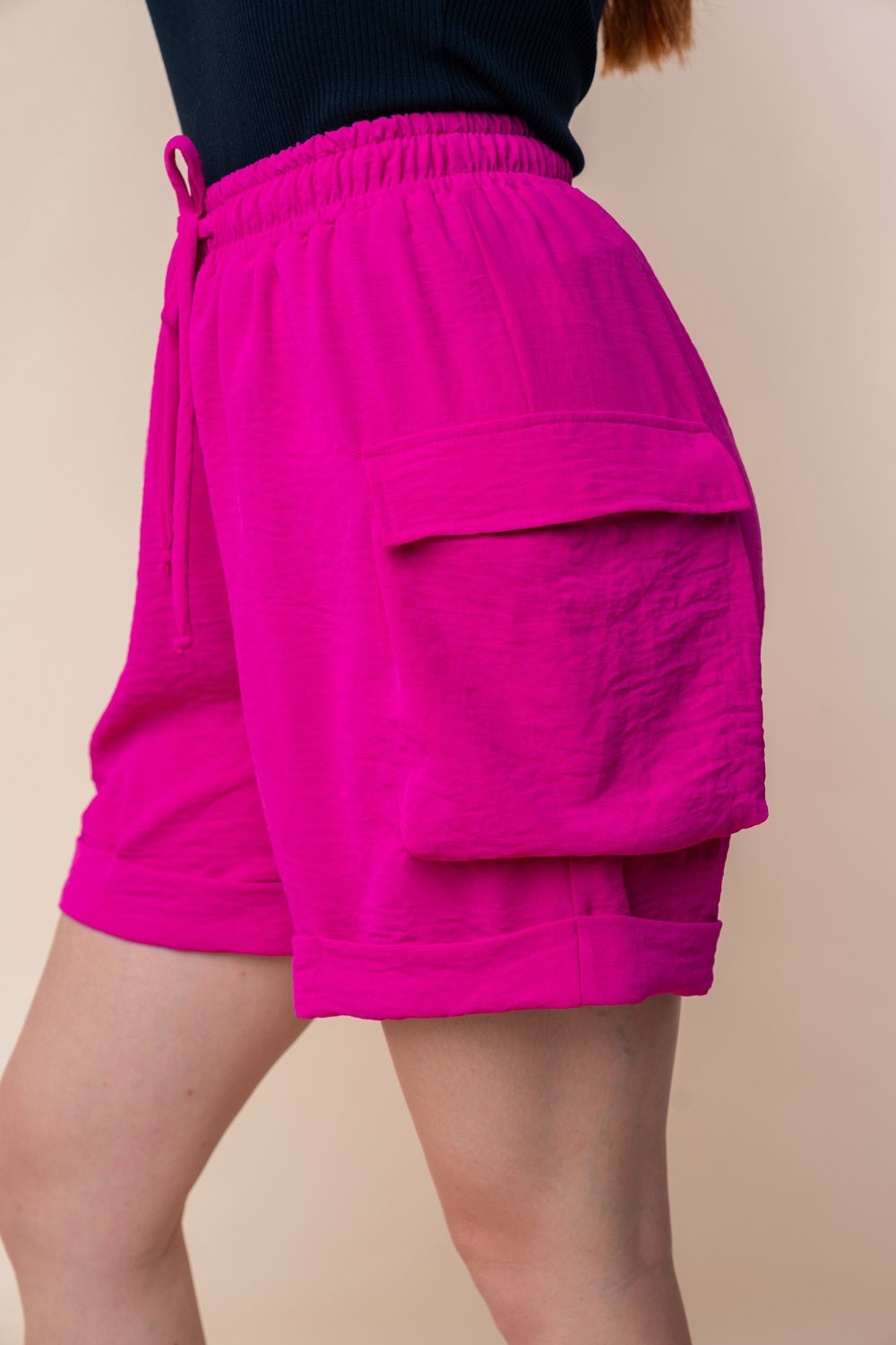 A person is wearing the White Birch High Waisted Drawstring Knit Cargo Shorts in bright pink, featuring side pockets and a drawstring waistband.