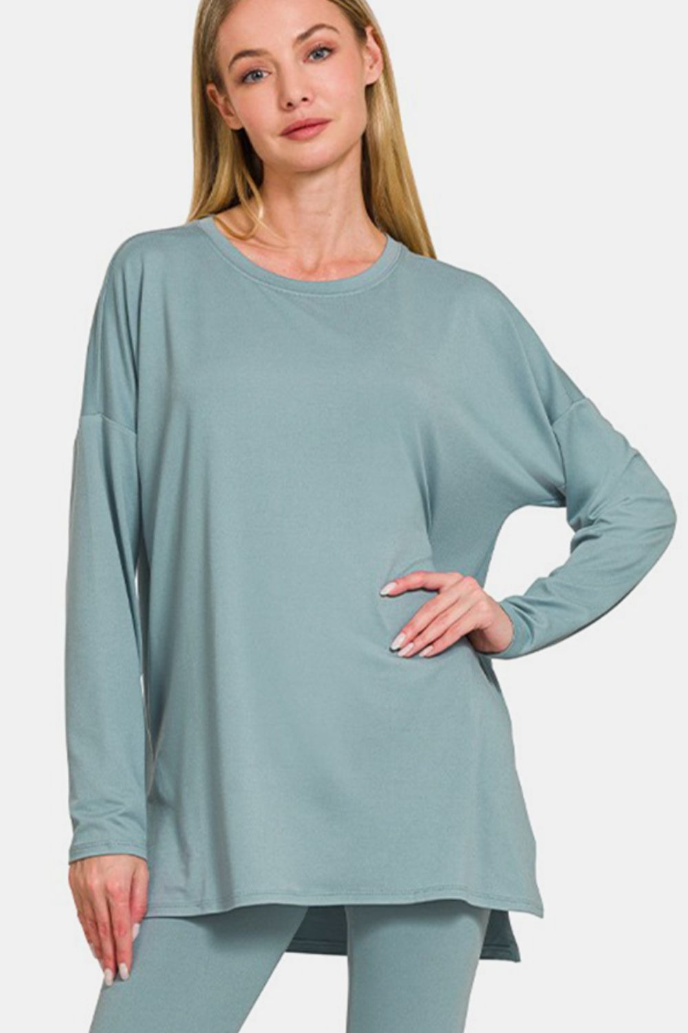 A person wearing the Zenana Full Size Brushed Microfiber Top and Leggings Lounge Set, featuring a loose-fitting teal long-sleeve top and matching stretchy leggings, paired with black sandals, poses against a plain background.