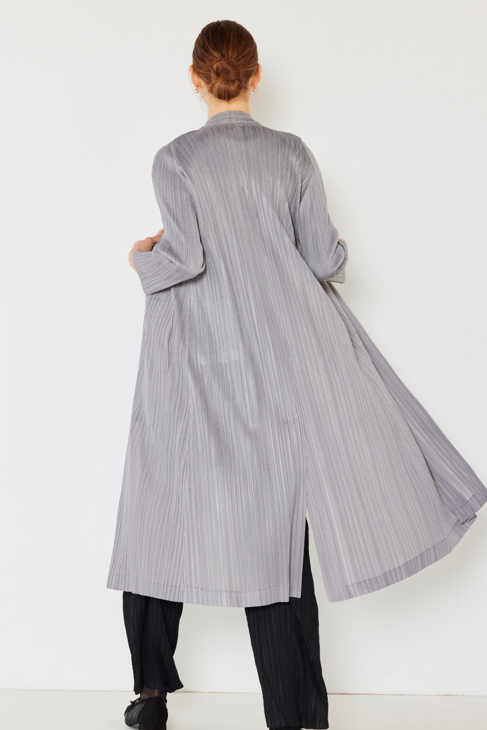 A person wears the Marina West Swim Pleated Long Sleeve Cardigan over a matching top and gray wide-leg pants, standing against a plain light background. This versatile layering piece, with its chic pleated long sleeves, adds an elegant touch to the ensemble.