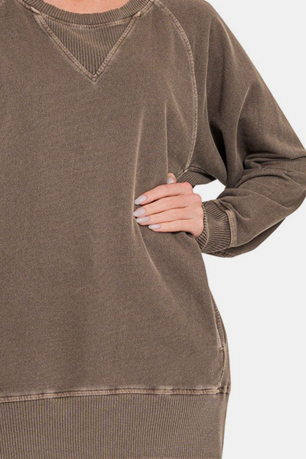 A woman wearing the Zenana Round Neck Long Sleeve Sweatshirt in beige and blue jeans stands with one hand on her hip against a neutral background.