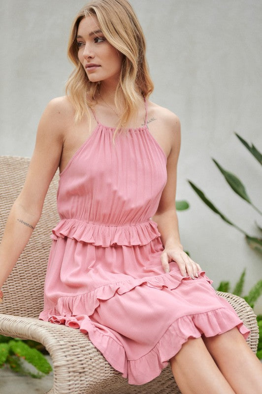 Wearing the Solid Ruffle Sleeveless Mini Dress in blue, the individual near the plants and wicker chair exudes elegance, making it an ideal choice for a casual brunch ensemble.