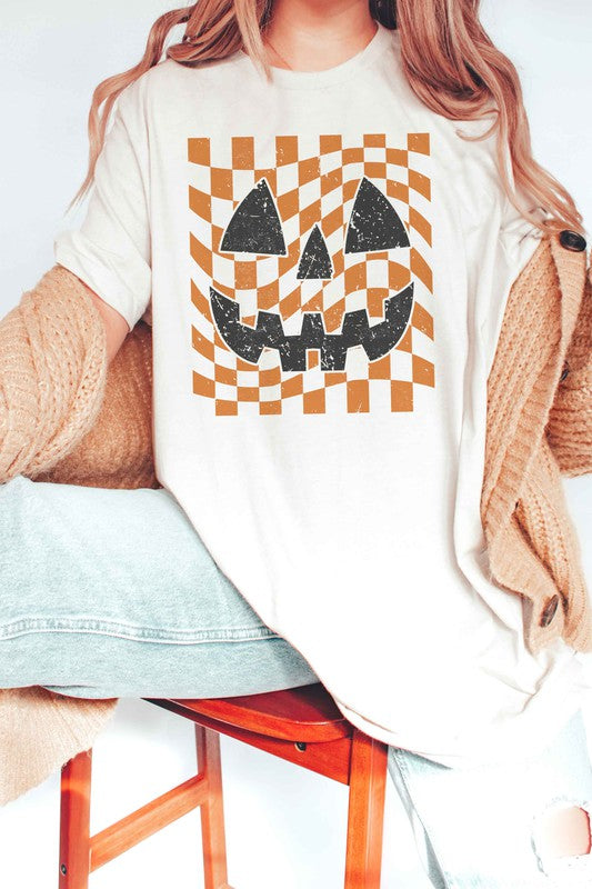 Person wearing a CHECKER PUMPKIN FACE Graphic Tee, made from 100% cotton, paired with high-waisted blue jeans.