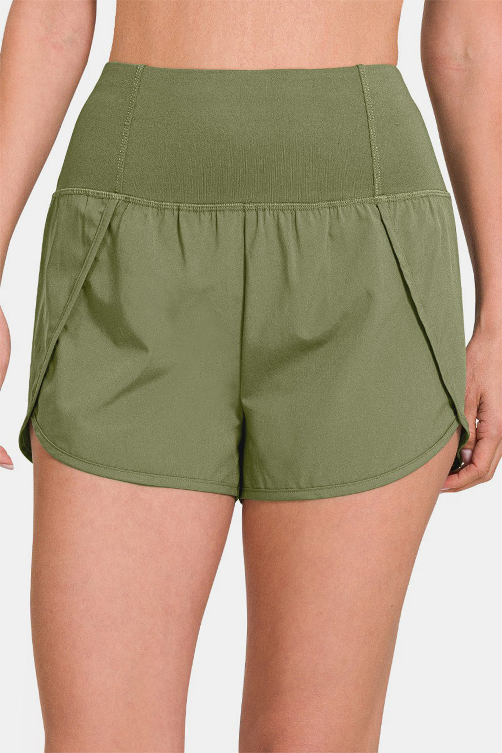 Individual sporting Zenana High-Waisted Zippered Back Pocket Active Shorts in light green, featuring a wide waistband, side slits, and a convenient zippered back pocket—ideal for active wear.