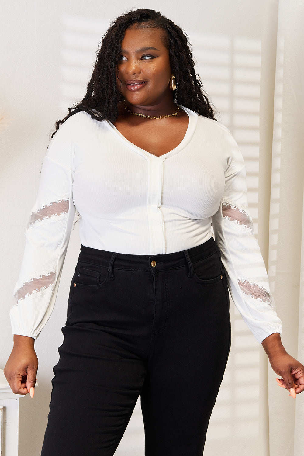 A woman wearing a Double Take V-Neck Dropped Shoulder Blouse with lace detail and black pants stands in front of a light-colored background.