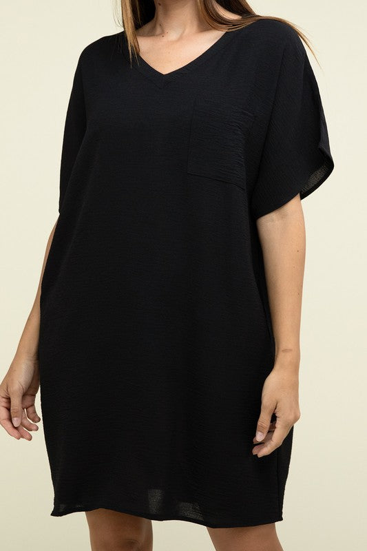 A woman wearing a loose light brown Woven Airflow V Neck T-Shirt Dress with Pockets stands against a plain background. Made from breathable fabric, this summer dress includes pockets where her hands rest as she smiles slightly.