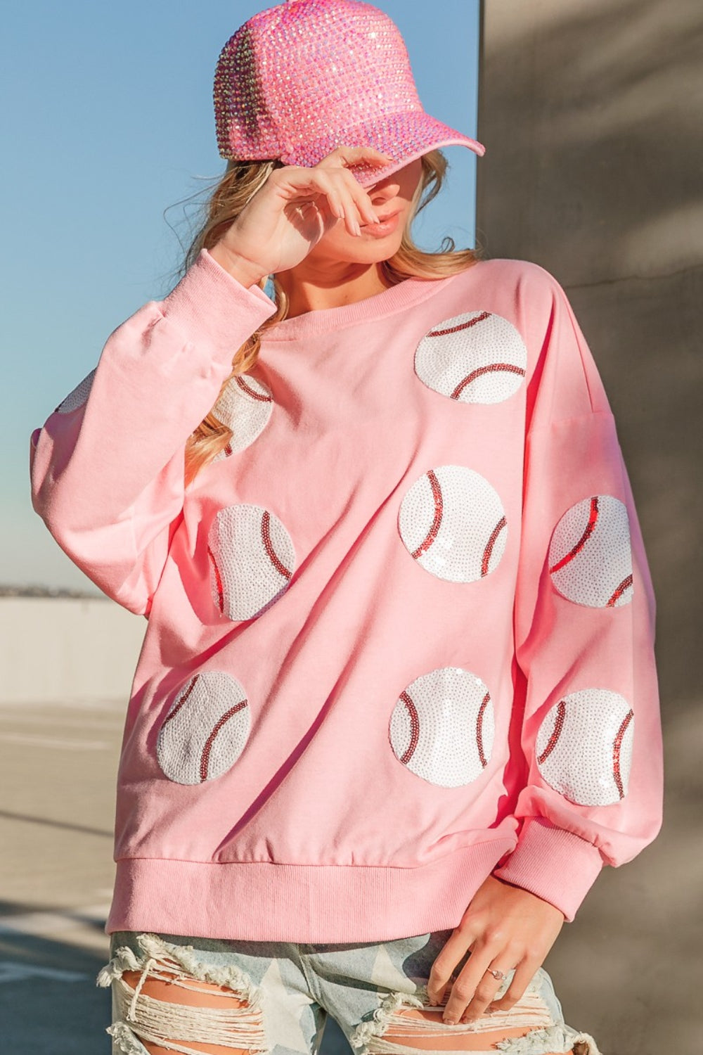 Person wearing a trendy and eye-catching pink sequin cap and the BiBi Sequin Baseball Patches French Terry Sweatshirt, standing in outdoor daylight.