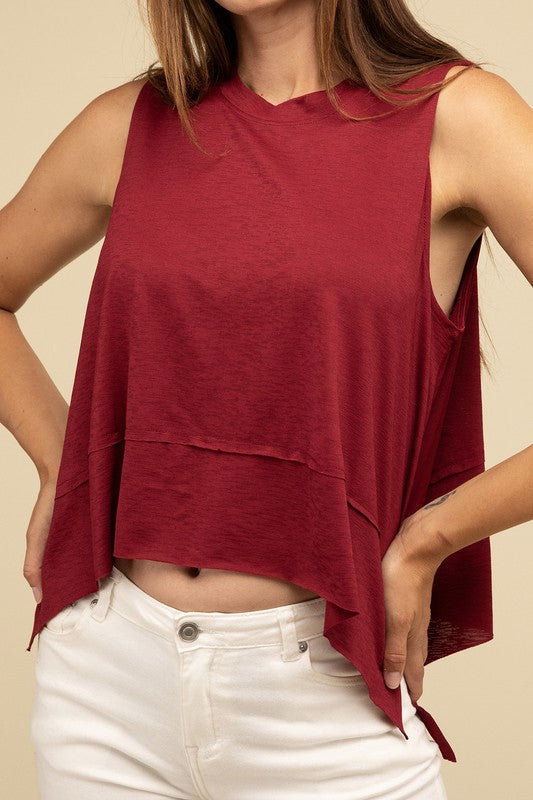 Wearing the Shark Bite Side Slit Short Sleeveless Top in maroon paired with white pants, a model is set against a beige background, exemplifying an effortlessly chic and casual wardrobe.