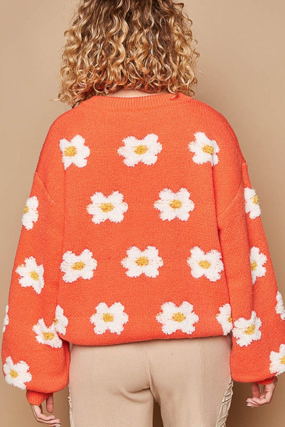 A person is wearing the POL Daisy Pattern Drop Shoulder Sweater, featuring an oversized fit and charming daisy design, standing against a beige background.