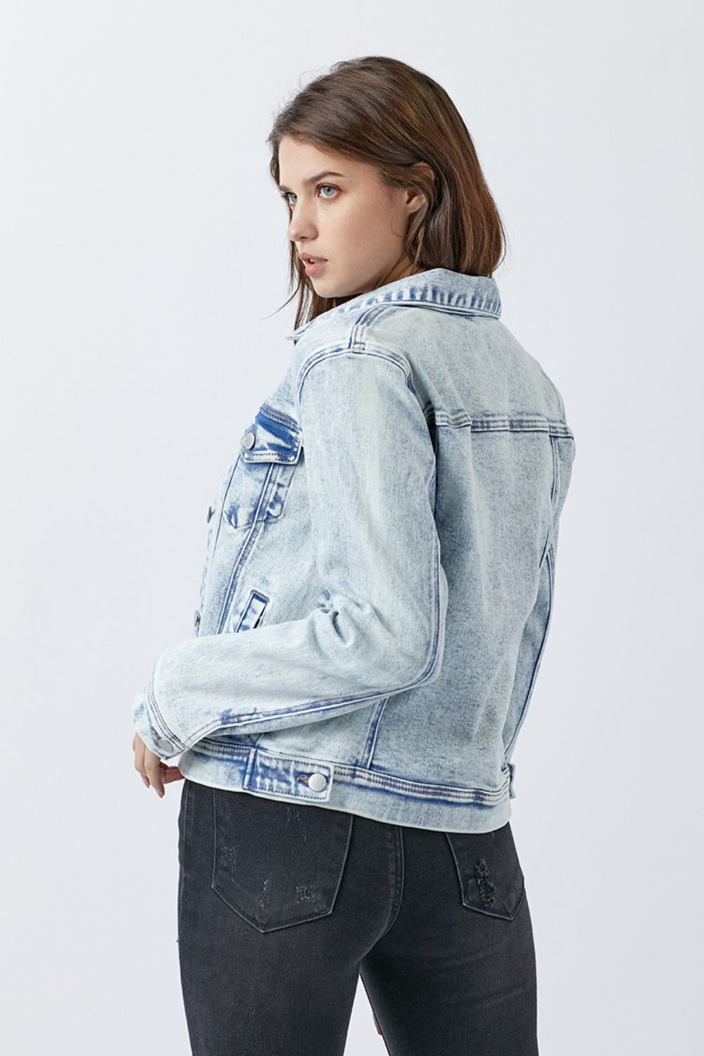 A woman wearing the RISEN Button Up Washed Denim Jacket over a white top and black jeans, standing against a plain background.