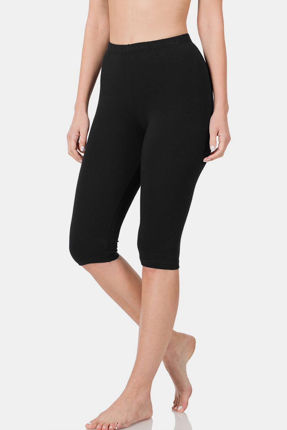 A person is standing barefoot wearing Zenana Full Size High Waist Capris, black knee-length leggings with a flattering fit, against a plain white background.