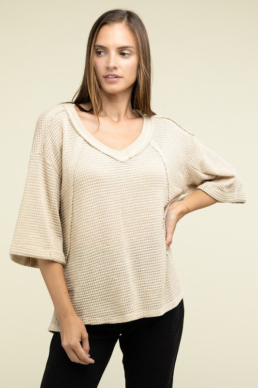 A person is dressed in a Brushed Waffle Exposed-Seam 3/4 Sleeve Top and white shorts, perfect for a casual wardrobe. They stand against a plain background, effortlessly embodying relaxed style.