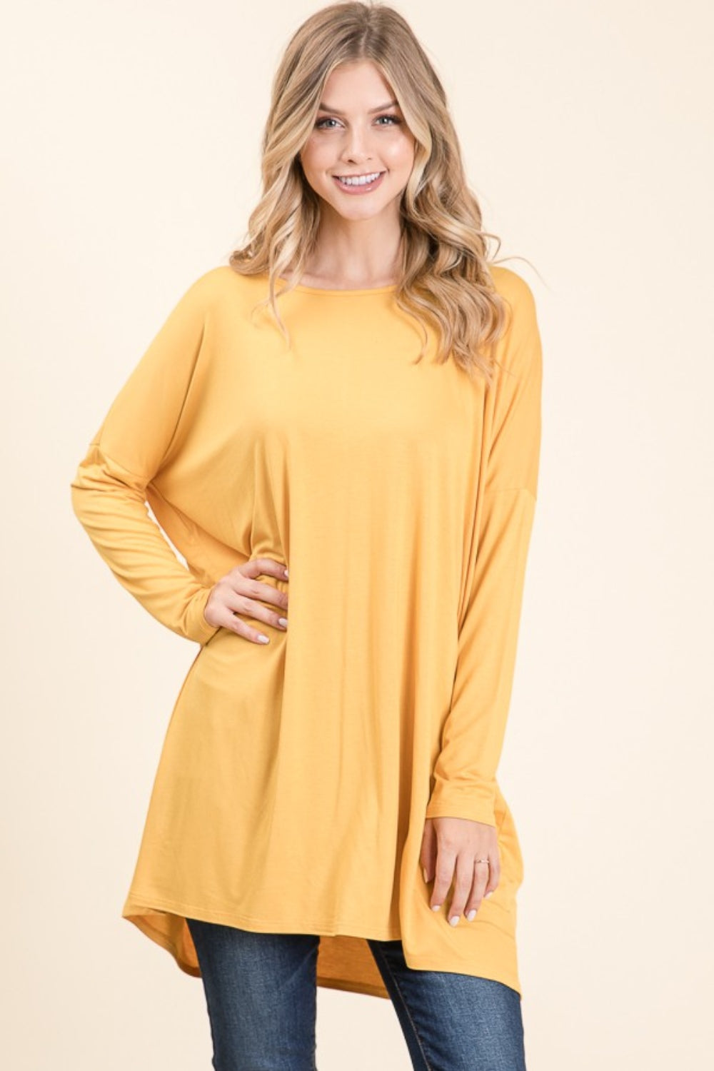 A woman with long blonde hair is wearing a versatile and comfortable, loose-fitting BOMBOM Round Neck Long Sleeve Oversized Top in yellow and blue jeans. She is smiling and standing against a plain light background.