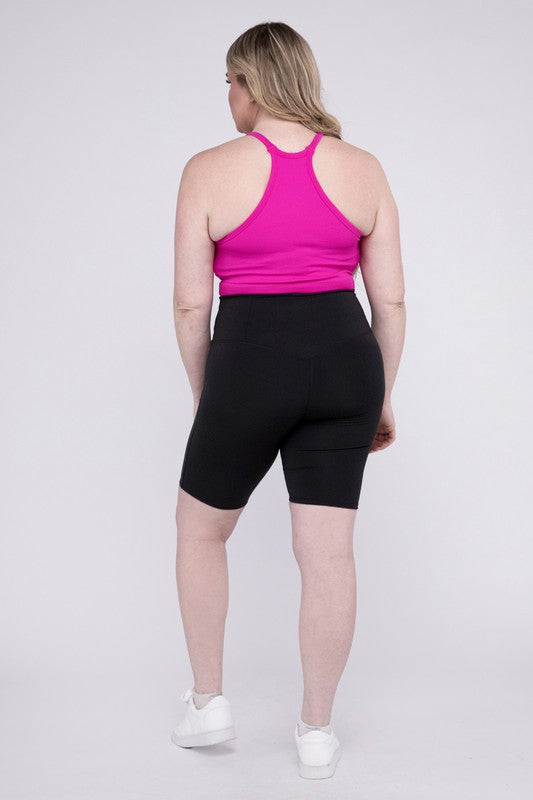 Against a plain background, a person showcases the Plus Athletic High Rise Biker Shorts in coral, crafted from high-quality athletic fabric and paired with a pink top.