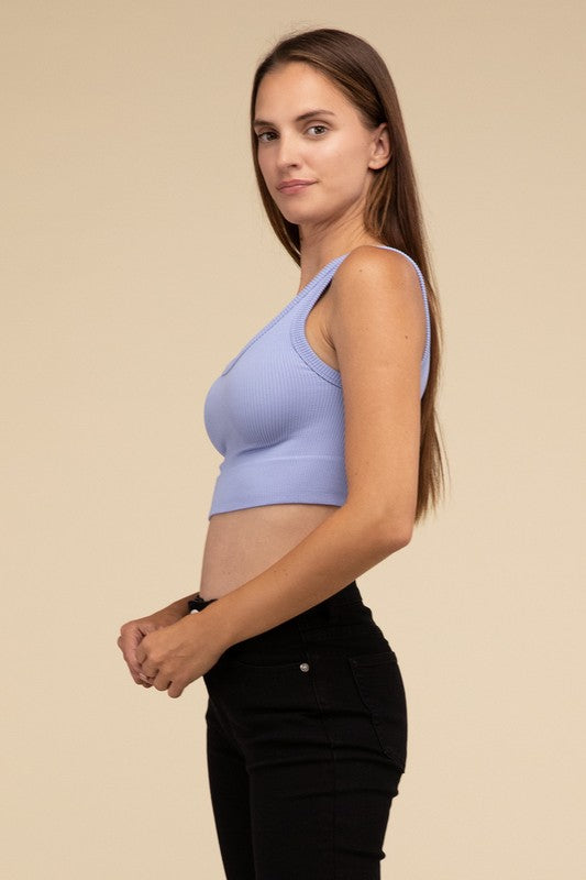 A person with long brown hair wearing the Ribbed Seamless Crop Top in light blue and black pants stands against a beige background, showcasing a perfect summer essential.