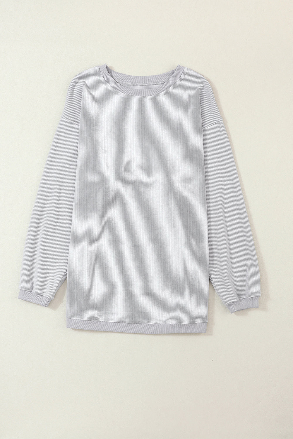A woman wearing the Light Grey Ribbed Corduroy Oversized Sweatshirt with loose long sleeves, designed in corded fabric, making it fashionable for all body shapes.