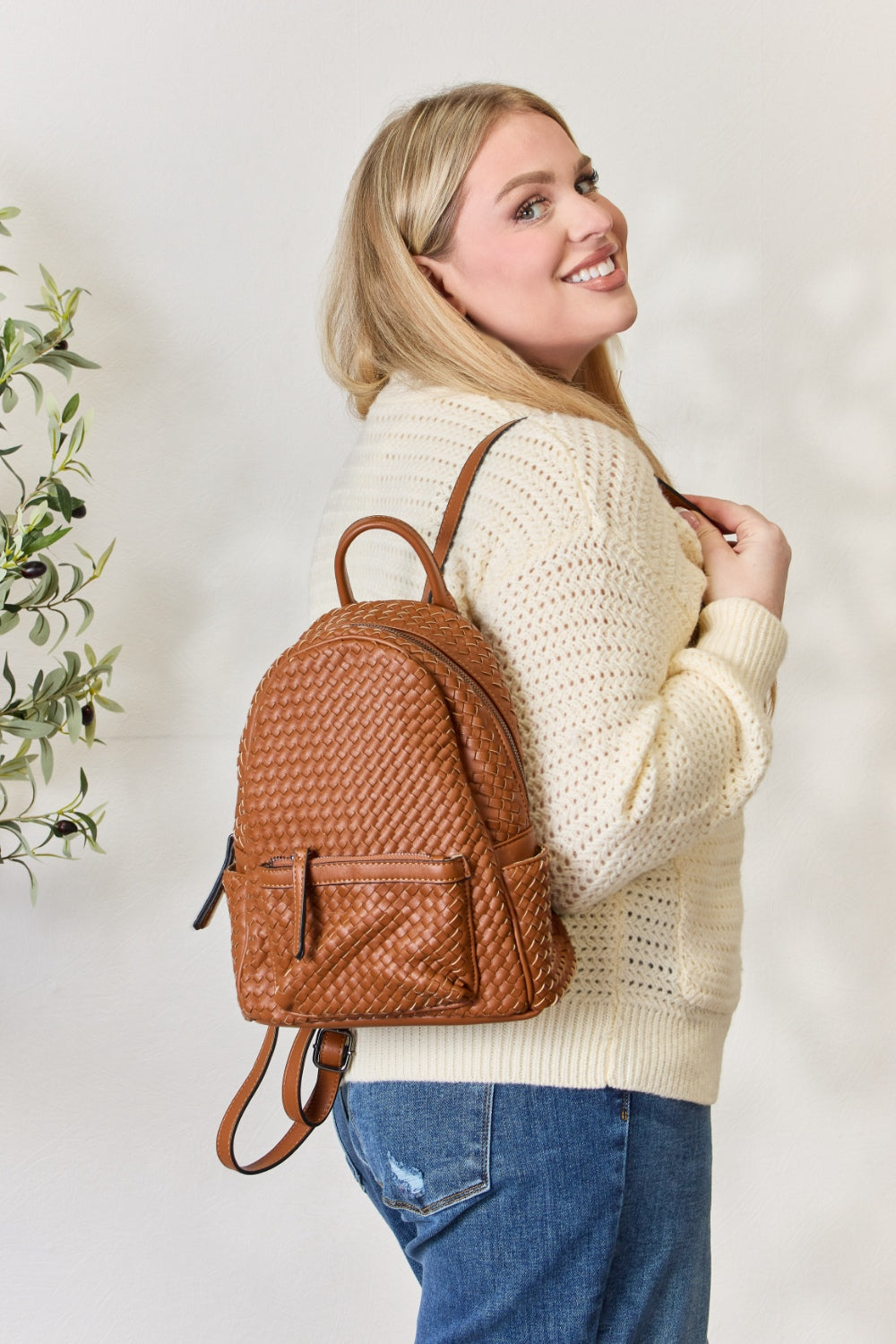 A person wearing a cream sweater and jeans is carrying the SHOMICO PU Leather Woven Backpack in brown.