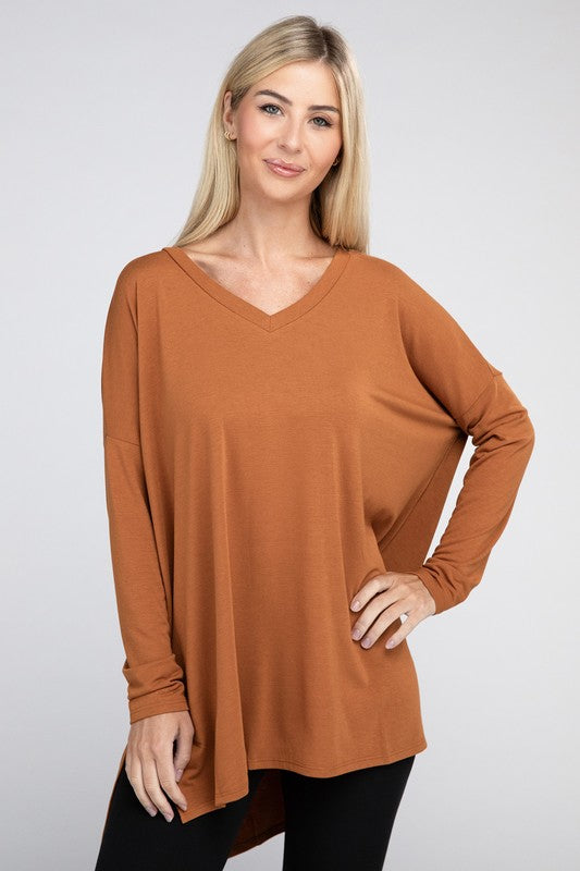 A woman with long, blonde hair is wearing a loose-fitting, brown Dolman Long Sleeve V-Neck Side Slit Hi-Low Hem Top and black pants. She poses with one hand on her hip and a neutral facial expression against a light grey background.