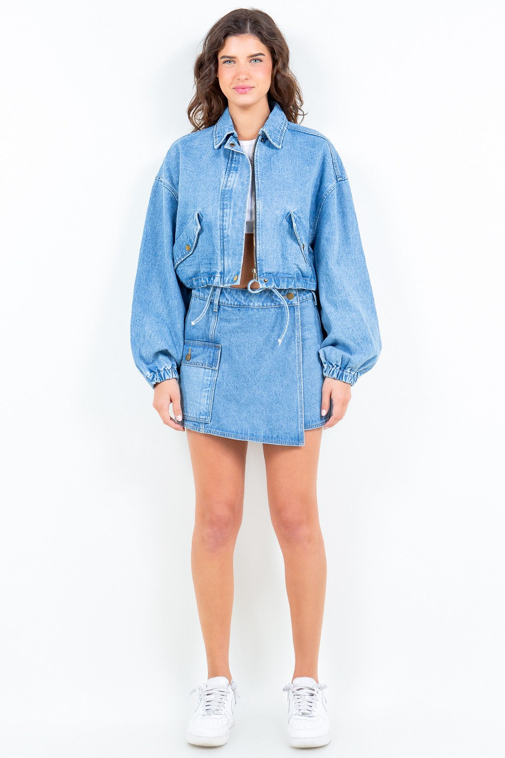 A woman wearing the American Bazi Drawstring Waist Crop Denim Jacket in light blue denim and a matching skirt, standing against a plain light background.