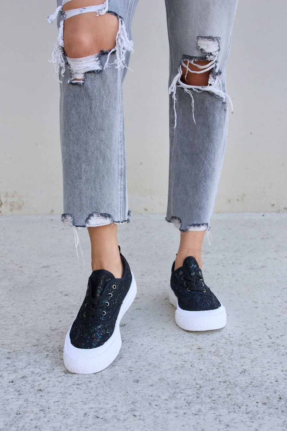 Person wearing ripped gray jeans and Forever Link Sequin Lace-Up Platform Sneakers.