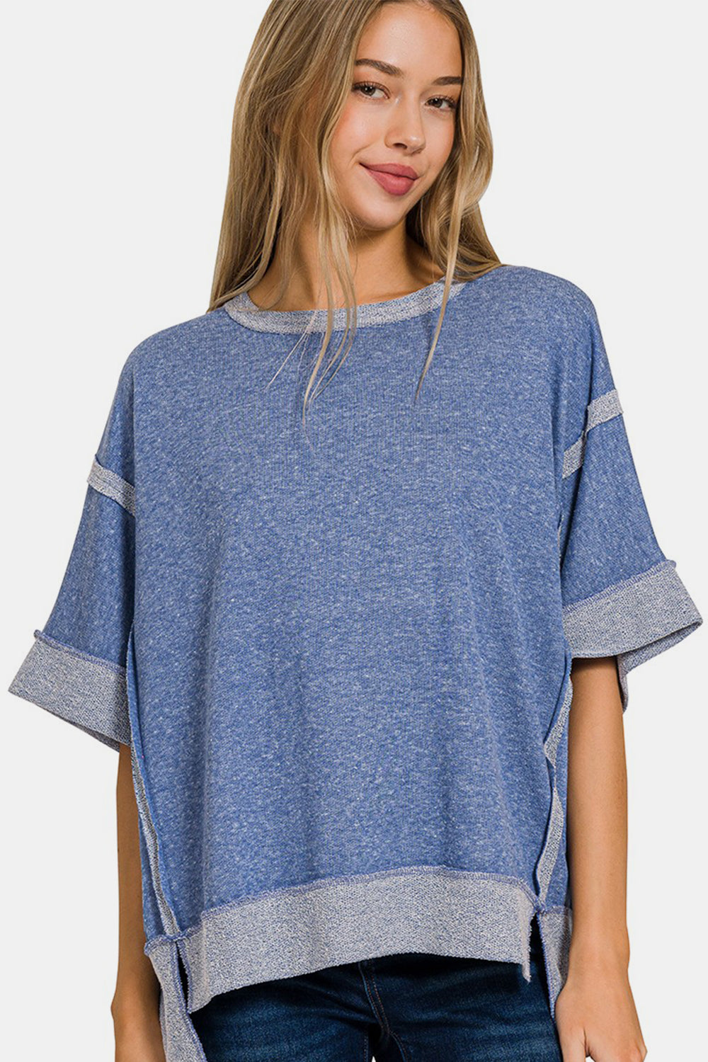 A smiling woman with light blonde hair is wearing a Zenana Contrast Trim Drop Shoulder T-Shirt, featuring grey contrast trim on the sleeves and hem, paired with casual blue jeans.