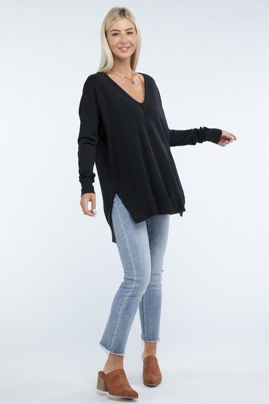 A person wearing a Hi-Low Hem Front Seam Sweater in brown and light blue jeans stands with hands partly in pockets. The individual has long hair and wears a necklace.