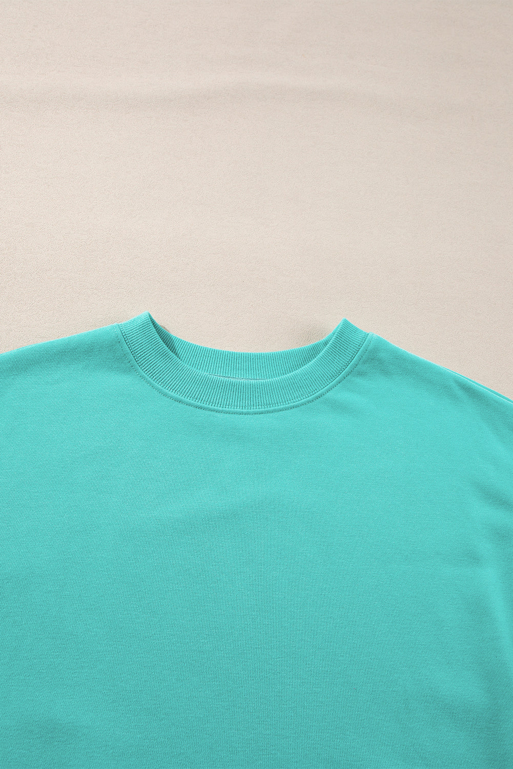 Person with long hair wearing an Aruba Blue Plain Drop Shoulder Crewneck Pullover Sweatshirt and carrying a floral crossbody bag, seen from the back, walking outdoors.