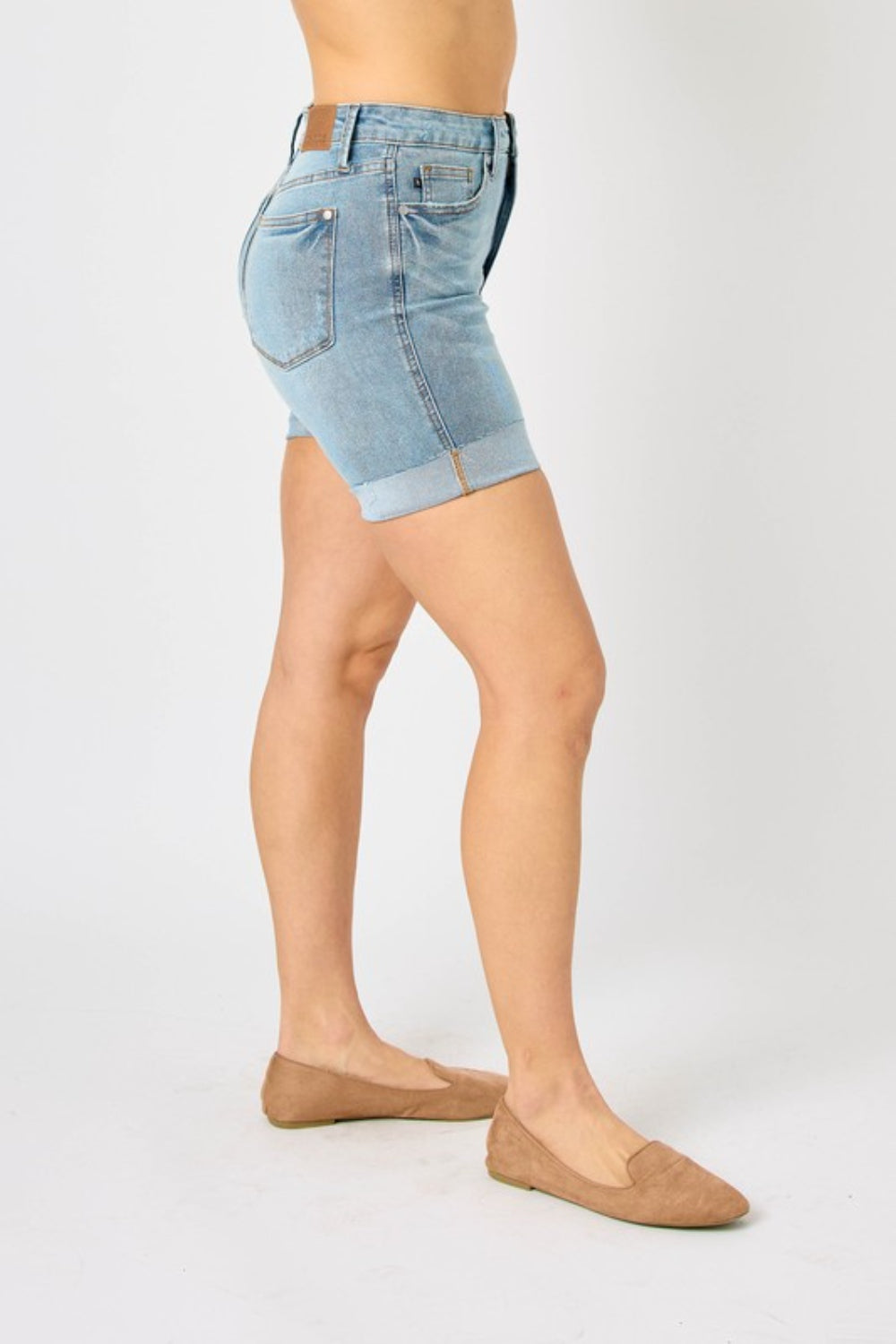 Person wearing Judy Blue Full Size Tummy Control Denim Shorts, which have a flattering fit, paired with brown shoes against a plain white background.