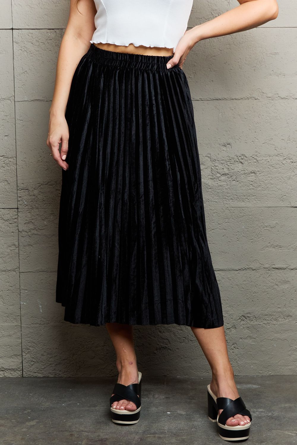 Person wearing a white sleeveless top, an elegant Ninexis Accordion Pleated Flowy Midi Skirt, and black platform sandals stands against a textured gray wall.