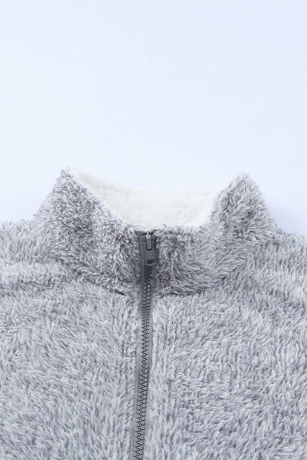 A woman with wavy hair in a Grey Zip Neck Oversize Fluffy Fleece Pullover and jeans holds a metal tumbler, facing away from the camera against a plain background. The cozy oversize fit of her ultra-soft pile fleece outerwear exudes comfort and style.