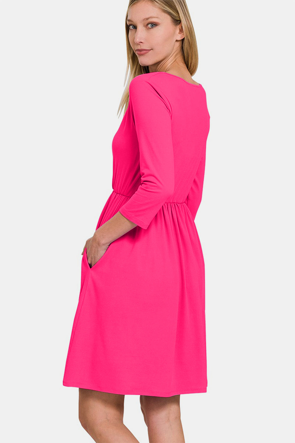 A woman in a pink Zenana Three-Quarter Sleeve Surplice Dress with Pockets stands against a white background.