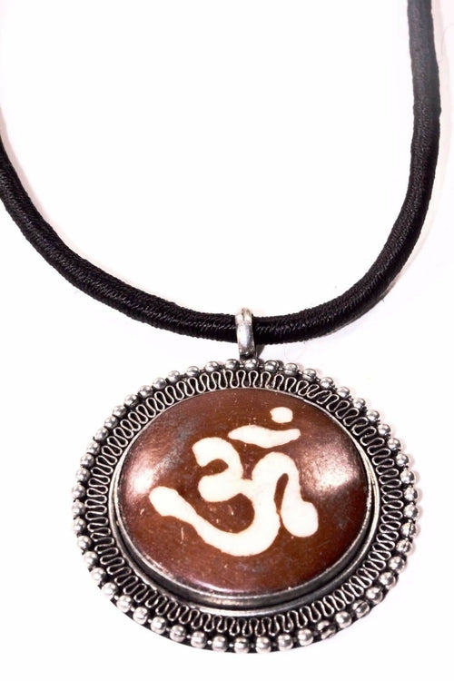 The Auspicious Om Spiritual Necklace, with a black cord and a round pendant featuring an Om symbol on a brown background framed by a decorative silver border, embodies boho-chic elegance.