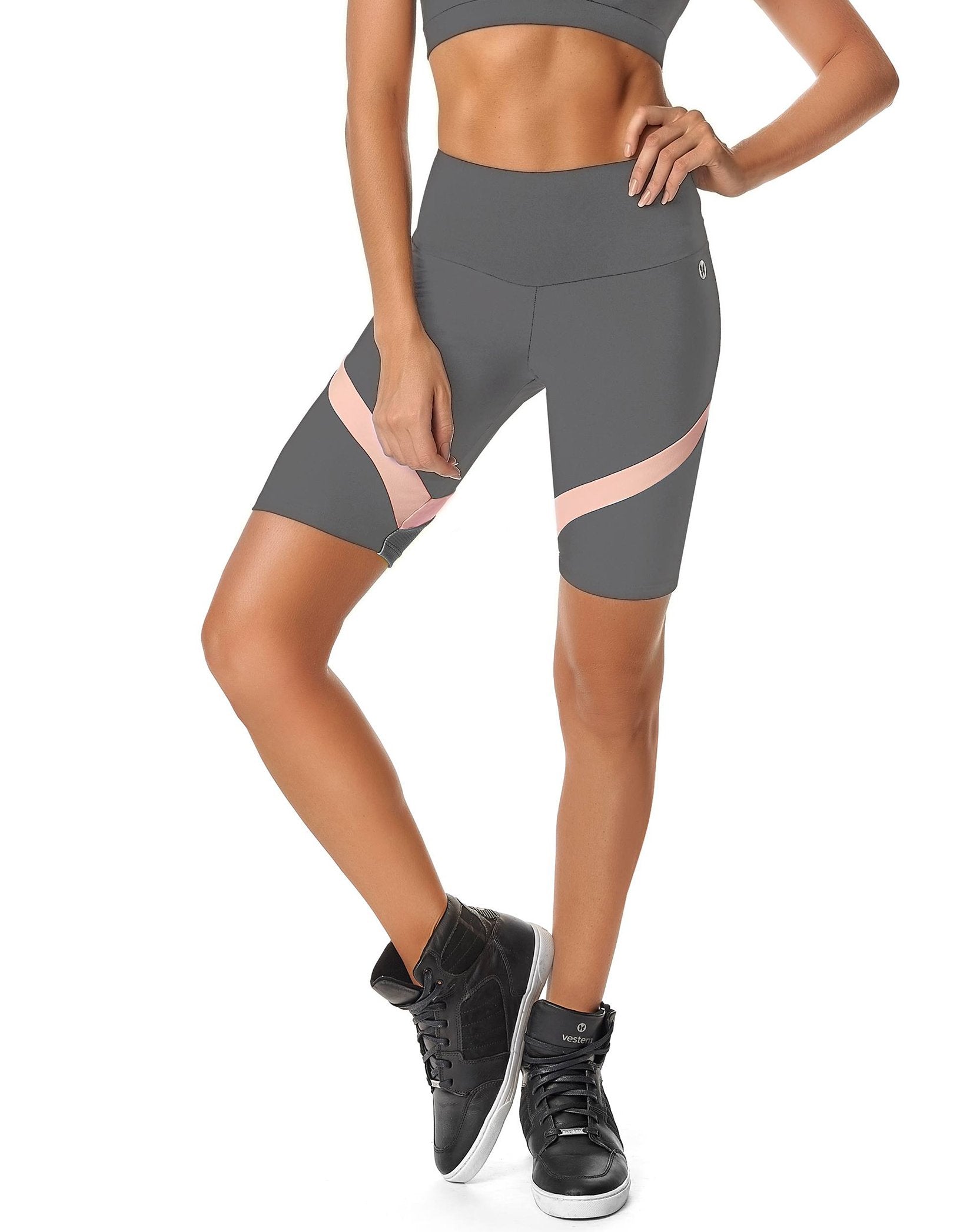 A person in a black sports bra and Calle Ocho Women Biker Shorts with white stripes, made from sweat-wicking fabric for ultimate comfort, poses with one hand on their hip. They sport black high-top athletic shoes, ideal for any fitness activity.