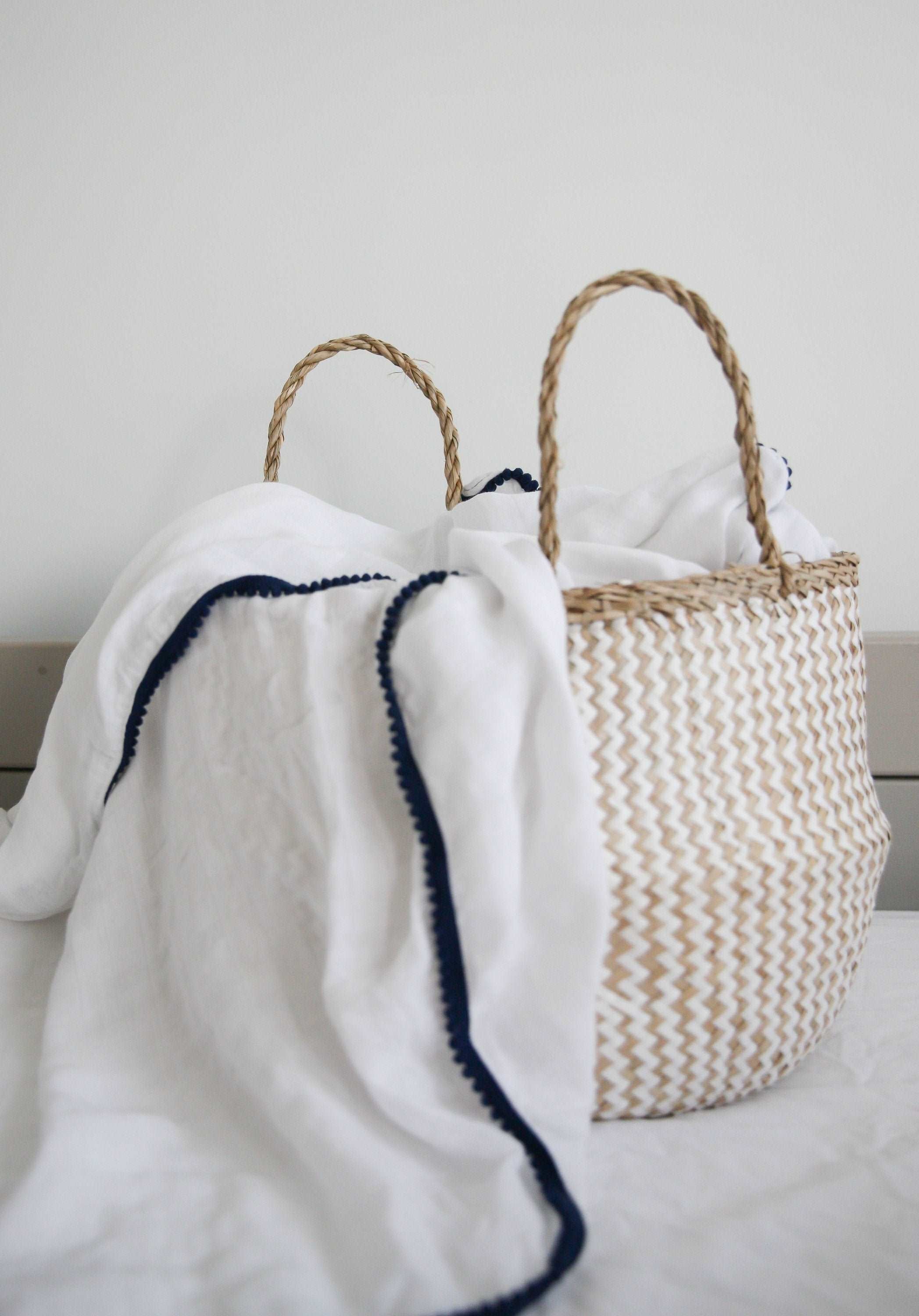 A white 3 Pc Newborn Essential Set - Hooded Towel, Swaddle + Toy Rattle by Ivory Meleager on top of a bed.