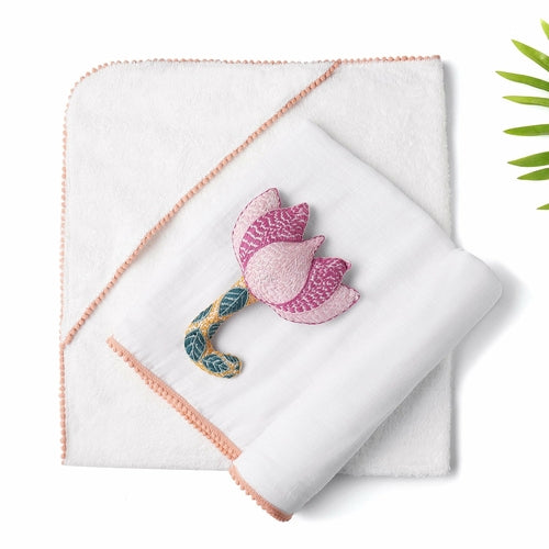 A white 3 Pc Newborn Essential Set - Hooded Towel, Swaddle + Toy Rattle by Ivory Meleager on top of a bed.