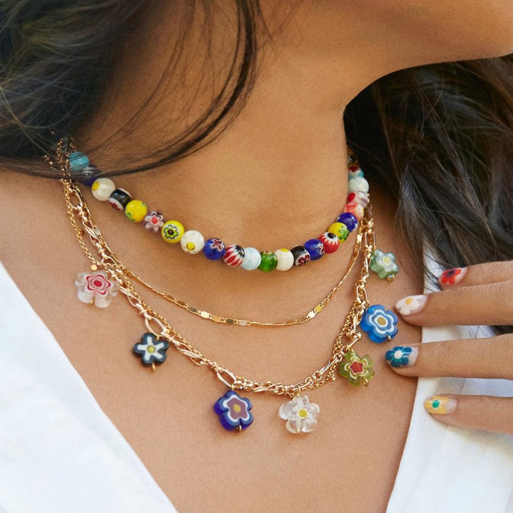 Close-up of a woman wearing a Candice Layered Multi-Color 2 PC Layered Necklace and showing off a flower pendant, with painted nails resting on her collarbone.