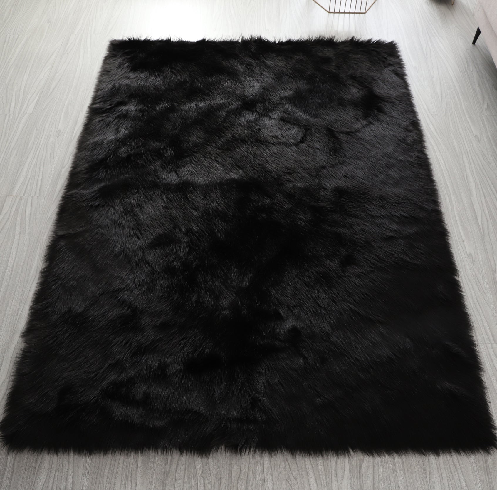 A modern living room featuring a large, Cozy Ultra Soft Fluffy Faux Fur Black Area Rug with an open book on it, a tan sofa, and a side table with a potted plant, against a backdrop of sheer